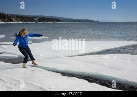 Erwachsenen blonde Frau trägt einen Mantel und Stiefel behutsam Schritte auf einer riesigen Eisscholle schweben am Lake Superior Stockfoto
