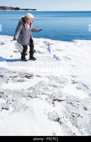 Erwachsene kaukasischen Frau in 40er Jahren herüber sorgfältig eisigen Schnee entlang der gefrorenen Ufer des Lake Superior im Winter, zwei Häfen, MN Stockfoto