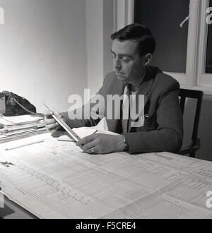 1950er Jahre historische, Erwachsene männliche Büroangestellter sitzt an seinem Schreibtisch, große Papierkarten zu studieren. Stockfoto