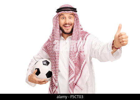 Studioaufnahme von einem jungen arabischen Mann hält einen Fußball und geben einen Daumen oben isoliert auf weißem Hintergrund Stockfoto