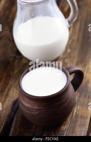 Milch in Keramik Tasse und Glas Krug auf Holztisch Stockfoto