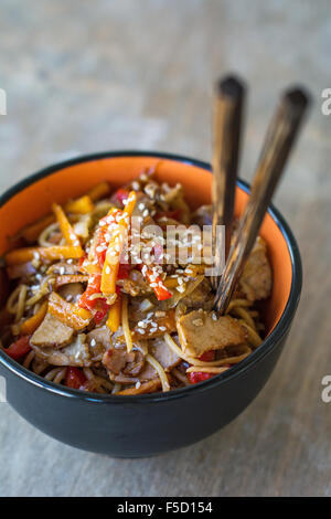 Pfannengerichte mit Gemüse und Fleisch, garniert mit Sesam in Schüssel mit Stäbchen. Traditionelle asiatische Küche Stockfoto