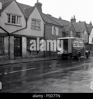 1950er Jahre historische, Verkäufer für immer bereit gesehen stehen vor seinem Bus unterwegs zu liefern an Kunden, kleine Hautpstraße Ladengeschäft. Stockfoto