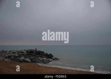 Entfernte Figur meditieren auf Felsen durch ruhige See, Sussex Stockfoto