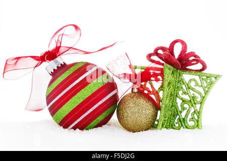 Weihnachtskugeln rot und gold mit rotem Band und ein grünes Geschenk auf dem Schnee. Stockfoto