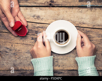 Frau hält, dass Kaffee und Mann gold Ring als Geschenk für Geburtstag oder Engagement gibt Stockfoto
