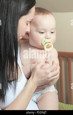 Hingebungsvolle Mutter Sohn Festlegung in Krippe für Nickerchen im Schlafzimmer Stockfoto