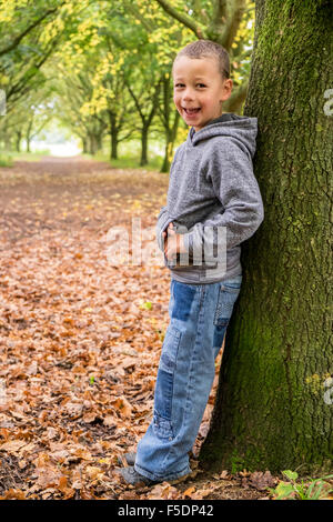 6 Jahre alten junge an einen Baum gelehnt lächelnd Stockfoto