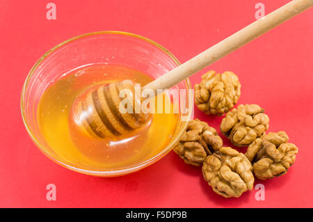 Geschälte Walnüsse und eine Schüssel mit Honig auf einem roten Tisch Stockfoto