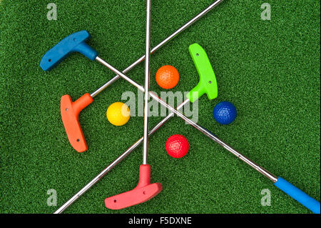 Vier Mini-Golf-Putter und Kugeln in sortierten Farben Verlegung Criss kreuzten auf Kunstrasen Stockfoto