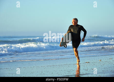 Applying Mann Joggen im Ozean Kante hält ein Surfbrett. Weiche frühen Morgenlicht wäscht über die herrliche Szenerie. Stockfoto