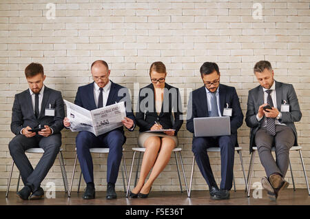 Moderne Business-Leute in eleganten Anzügen sitzen in Reihe entlang der Wand Stockfoto