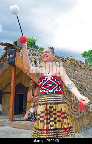 Maori-Frau und Maori-Mann in Te Puia Maori Village Rotorua. Frau tanzt mit POI(s), während der Mann in der Hütte dahinter ist. Nordinsel, Neuseeland Stockfoto