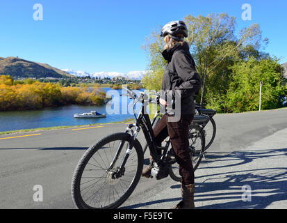 Lady Radfahrer auf einem Elektrofahrrad, E-Bike, auf die Landschaft am Ufer des Lake Wanaka, Frankton, Nr Queenstown, Südinsel, Neuseeland suchen Stockfoto