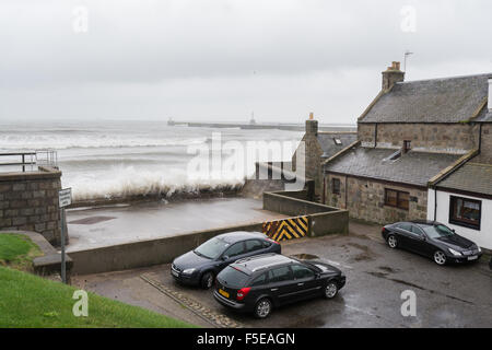 Wellen, die gegen Küstenschutzes vor der alten Granit Fischer Häuser und Autos, Footdee, Aberdeen, Schottland, UK Stockfoto