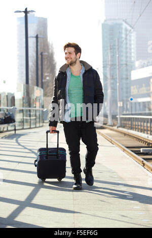 In voller Länge Portrait eines jungen Mannes mit Koffer am Bahnhof Bahnsteig lächelnd Stockfoto