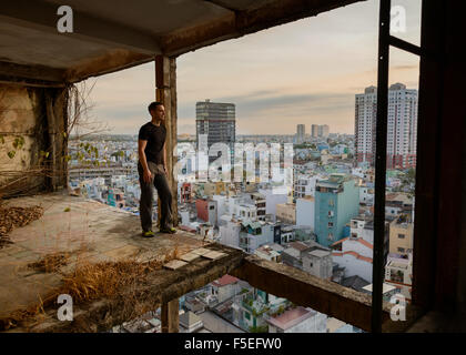 Mann in heruntergekommenen Gebäude, Blick auf Stadt, Ho Chi Minh, Vietnam Stockfoto