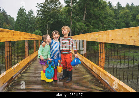 Zwei Jungs und ein Mädchen auf einer Holzbrücke im Regen stehen Stockfoto