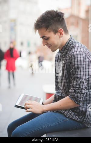 junge hübsche dunkle Alternativmodell Mann in der Stadt mit Tablet technologische Geräte von drahtlosen Stockfoto