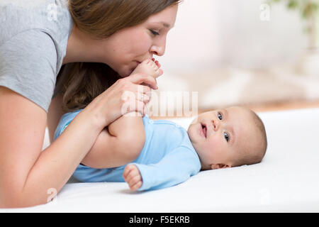 Mutter küsst Baby Tochter Füße beim Spielen auf einem weißen Bett Stockfoto