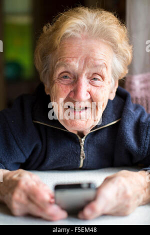 Alte Frau tippt auf Handy auf dem Tisch. Stockfoto