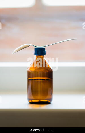 Eine Flasche Hustensaft mit einem Löffel in der Nähe des Fensters Stockfoto