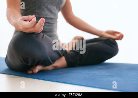 Nahaufnahme von weiblich Schneidersitz sitzen und die Hände auf die Knie während der Meditation. Frau sitzt in Lotus Pose auf Gymnastikmatte in Turnhalle Stockfoto