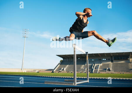 Professionellen männlichen Leichtathletin und Olympiateilnehmerin im Hindernislauf. Junge Sportler, die einen Sprung über eine Hürde beim Training auf der Rennstrecke Stockfoto