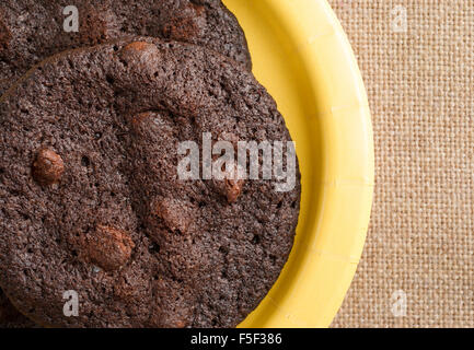 Enge Draufsicht der frisch gebackene Schokoladenkekse knusprig Brownie auf eine gelbe Pappteller auf Sackleinen Tischdecke Stockfoto