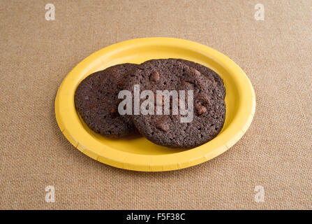 Drei gebackene frisch Schokoladenkekse knusprig Brownie auf eine gelbe Pappteller auf Sackleinen Tischdecke Stockfoto