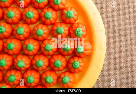 Enge Draufsicht von orange und grün Halloween Kürbis Süßigkeiten auf eine gelbe Pappteller auf Sackleinen Tischdecke Stockfoto