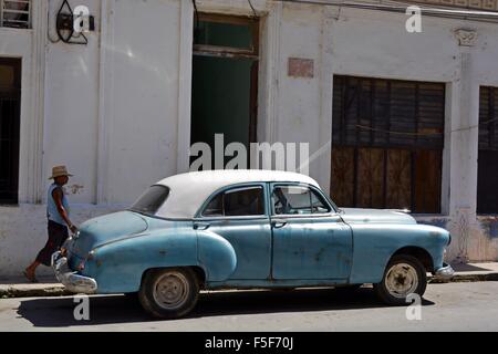 Kubanische Mann hinunter die Schattenseite einer sonnigen Straße vorbei an einem angeschlagenen blauen und weißen Oldtimer in Casablanca Havanna Kuba Stockfoto