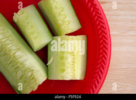 Mehrere Scheiben Gurken Stücke auf einer roten Platte oben auf einer hölzernen Tischplatte mit natürlichem Licht beleuchtet. Stockfoto