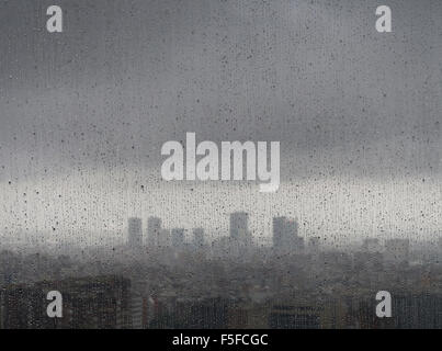 Nach starken Regenfällen entsteht die diffuse Skyline von Barcelona in der Dämmerung hinter Regentropfen auf ein Fenster. Stockfoto