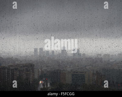 Nach starken Regenfällen entsteht die diffuse Skyline von Barcelona in der Dämmerung hinter Regentropfen auf ein Fenster. Stockfoto