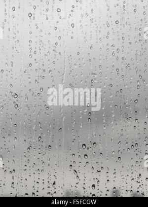 Nach starken Regenfällen sind viele Regentropfen ein Milchglas-Fenster nach unten rieselt. Unscharfe, traurig, Grau Himmel im Hintergrund. Stockfoto