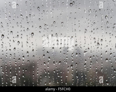 Nach starken Regenfällen sind viele Regentropfen ein Fenster nach unten rieselt. Diffuse Silhouette der Skyline einer Stadt entsteht in den Rücken. Stockfoto