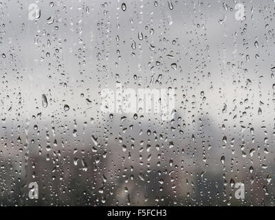 Nach starken Regenfällen sind viele Regentropfen ein Fenster nach unten rieselt. Diffuse Silhouette der Skyline einer Stadt entsteht in den Rücken. Stockfoto