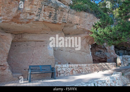 Bank unter massiven Kalkstein Felsformation mit Rissen und Trockenmauer an einem sonnigen Sommertag in Porto Cristo, Mallorca. Stockfoto