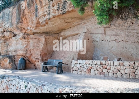 Bank unter massiven Kalkstein Felsformation mit Rissen und Trockenmauer an einem sonnigen Sommertag in Porto Cristo, Mallorca. Stockfoto