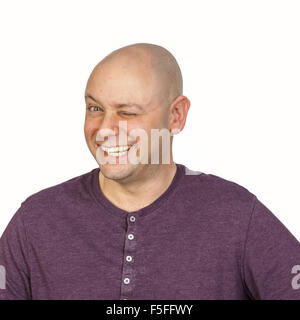 Big wink durch ein glatzköpfiger Mann im Studio auf weißem Hintergrund. Er trägt ein lila knöpfbare T-Shirt mit rundem Ausschnitt. Stockfoto