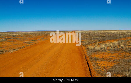 Lange rote Piste im australischen outback erstreckt sich über trockenen baumlosen Ebenen der Flinders Ranges Wüstenregion zum fernen Horizont & blauer Himmel Stockfoto