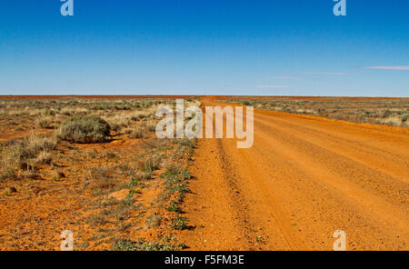 Lange rote Piste im australischen outback erstreckt sich über trockenen baumlosen Ebenen der Flinders Ranges Wüstenregion zum fernen Horizont & blauer Himmel Stockfoto