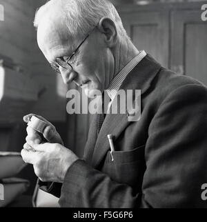 1950er Jahre historische, Mann mit Hilfe einer kleinen Lupe genau hinsehen, auf ein Objekt. Stockfoto