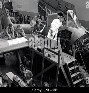 1960s, historisch, in einem Flugzeughangar, junge männliche Auszubildende im Bereich Luftfahrtingenieurwesen oder Studenten, die unter Aufsicht eines Ausbilders bei Short Brothers in Belfast, Nordirland, an einem Flugzeugmotor arbeiten. Stockfoto
