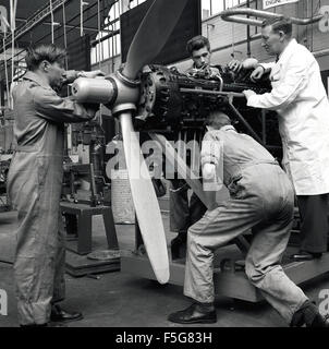 1950er Jahre, historisch, in einem Flugzeughangar, Flugzeugingenieurwesen oder technische Studenten arbeiten an einem Flugzeug Propeller und Motor unter Aufsicht von einem männlichen Lehrer in einem weißen Mantel. Stockfoto