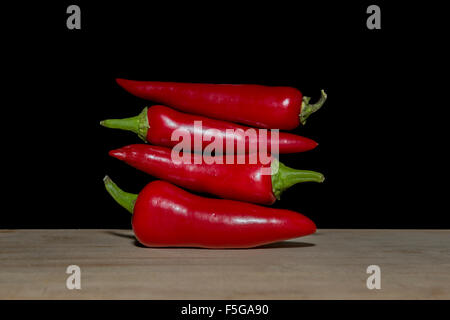 Turm aus roten Chilischoten auf ein Schneidebrett mit schwarzem Hintergrund Stockfoto