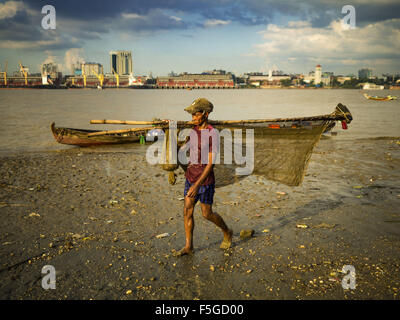 4. November 2015 - Dala, Yangon Division, Myanmar - Spaziergänge ein Fischer mit seinem Fang und Netze am Ufer des Flusses Yangon in Dala. Yangon ist im Hintergrund. Dala befindet sich am südlichen Ufer von Yangon River gegenüber dem Zentrum von Yangon, Myanmar. Viele Burmesen Leben in Dala und umliegenden Gemeinden und in zentralen Yangon für Arbeit über den Fluss gehen. (Kredit-Bild: © Jack Kurtz über ZUMA Draht) Stockfoto