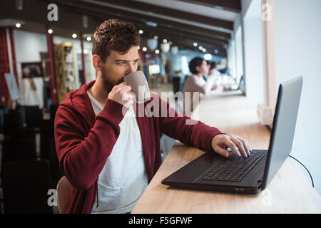 Moderne Mann in braun Hoodie Tee trinken und mit laptop Stockfoto