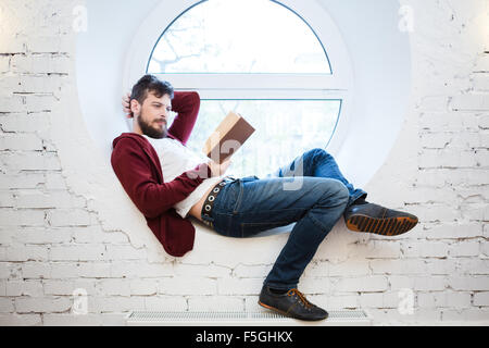 Schöne attraktive Student liegen und lesen auf weißen Fensterbank Stockfoto